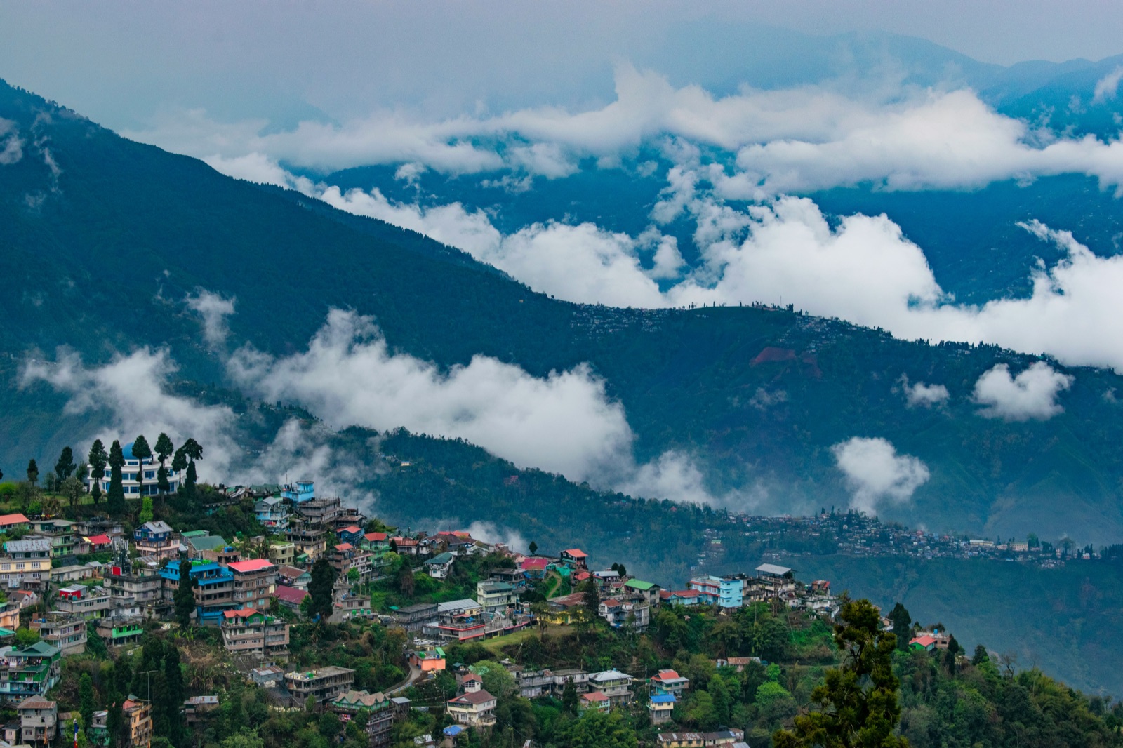 Clouds drifting between Darjeeling's ridge-top houses and the Himalayan foothills behind them