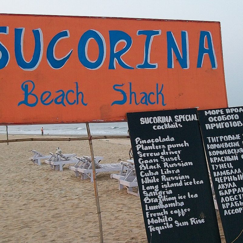 A hand-painted beach shack sign and cocktail menu on the sand at Colva beach, Goa