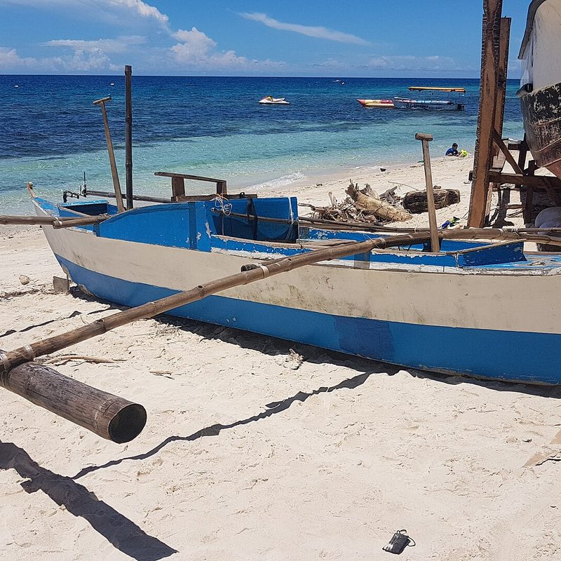 A traditional outrigger boat pulled up on white sand beside turquoise water