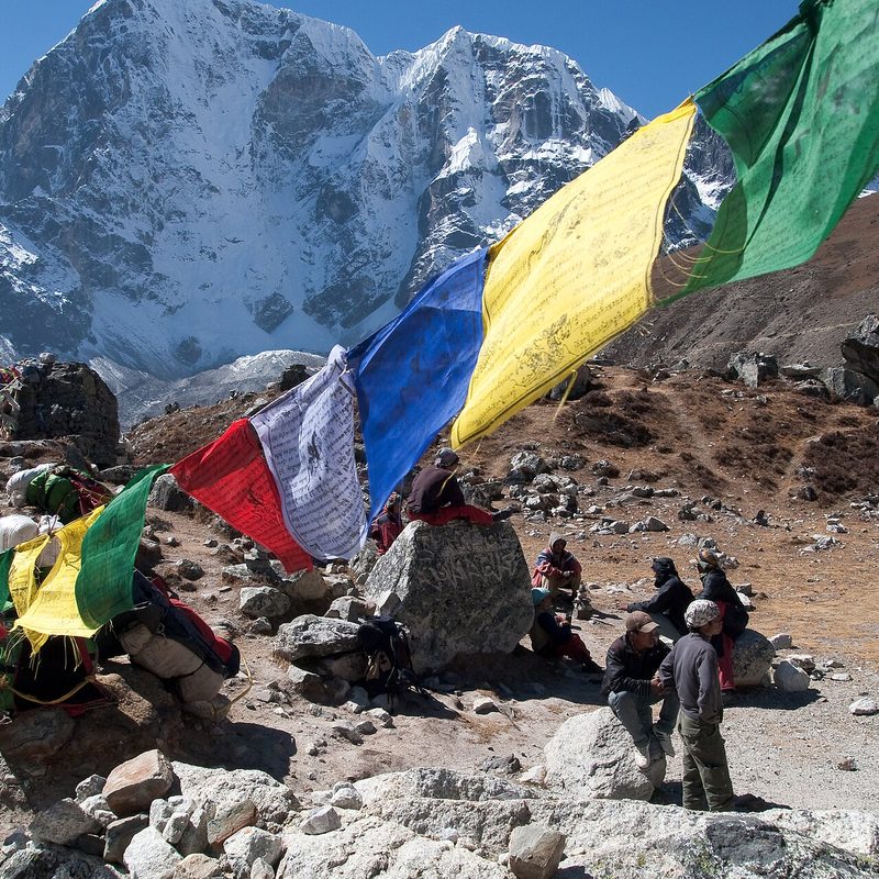 Prayer flags strung across a high Himalayan pass with trekkers resting below