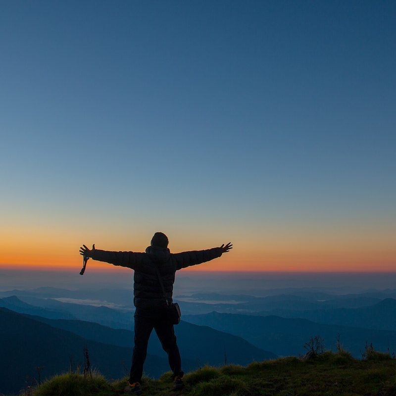A trekker standing arms-out against the sunrise over layered Himalayan ridges
