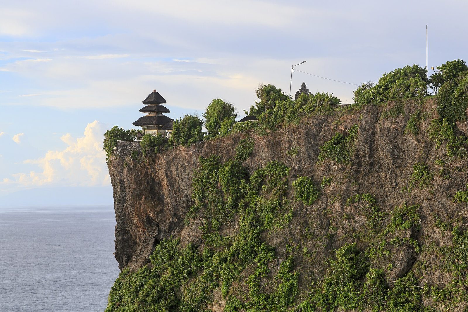 The Uluwatu temple on the edge of a green sea cliff above the Indian Ocean in Bali