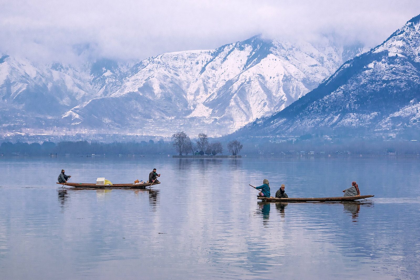 Shikara boats on the still water of Dal Lake below snow-covered mountains