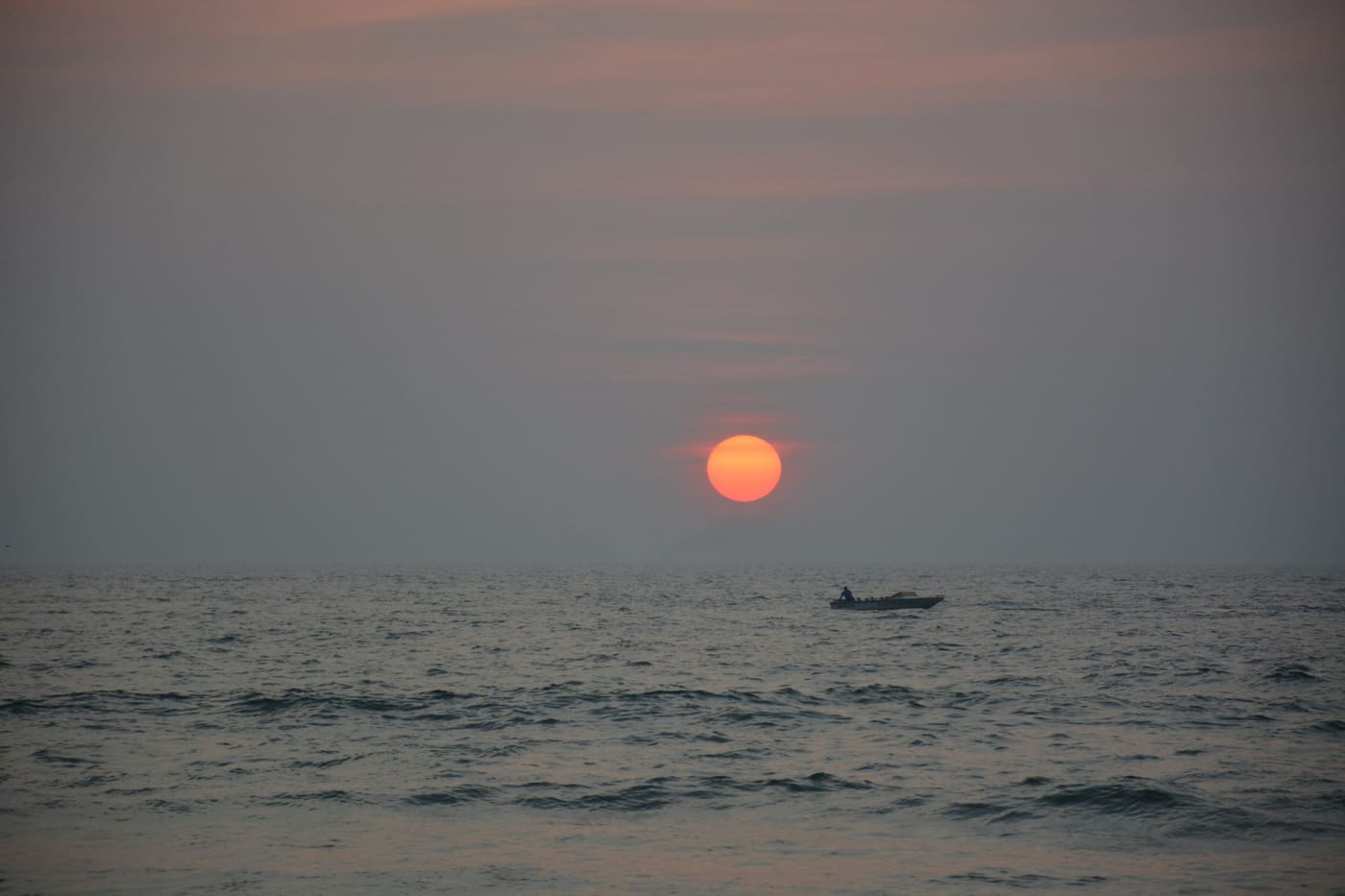 The sun dropping into the Arabian Sea with a small boat crossing the water beneath it