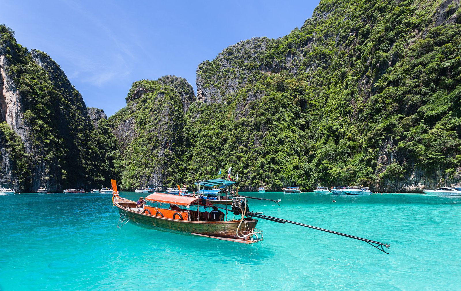 A longtail boat moored in the turquoise water of a limestone cove at Phi Phi Leh